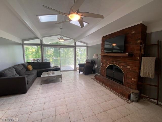 tiled living room featuring ceiling fan, vaulted ceiling with skylight, and a brick fireplace