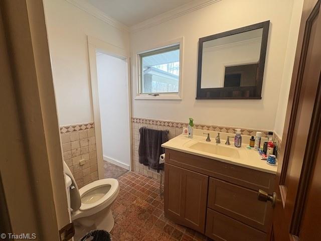 bathroom with tile walls, a wainscoted wall, crown molding, toilet, and vanity