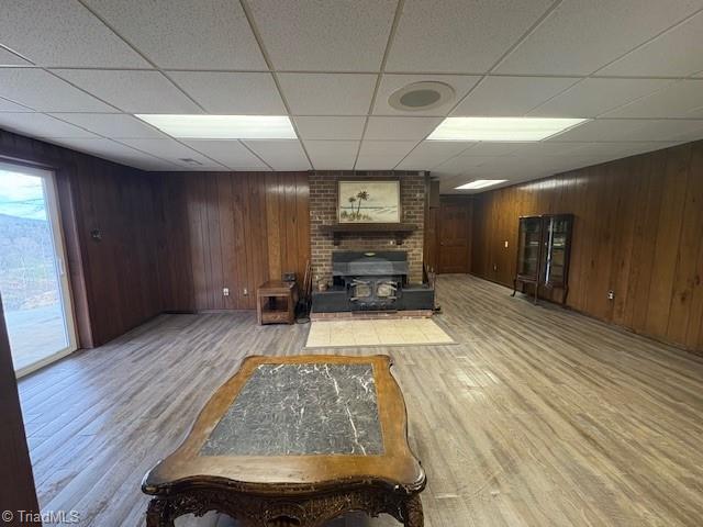 living room featuring a drop ceiling, light wood-style flooring, wood walls, and a fireplace