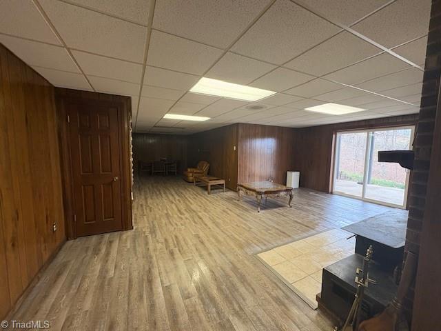 unfurnished living room with a drop ceiling, wood walls, and wood finished floors