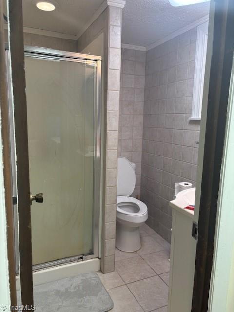 full bath with tile patterned flooring, crown molding, tile walls, and a shower stall