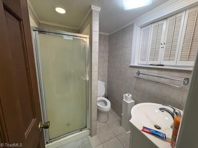 bathroom with toilet, a shower stall, a textured ceiling, tile patterned flooring, and tile walls