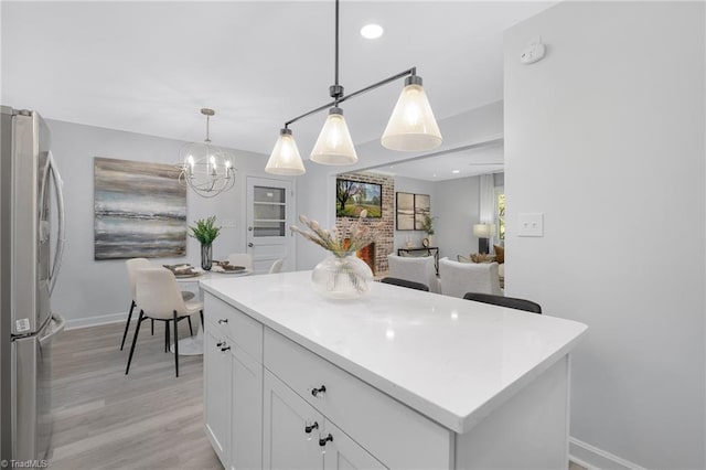 kitchen with white cabinets, a kitchen island, stainless steel refrigerator, light hardwood / wood-style flooring, and decorative light fixtures