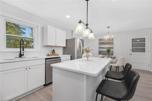 kitchen featuring hanging light fixtures, sink, a center island, white cabinets, and appliances with stainless steel finishes