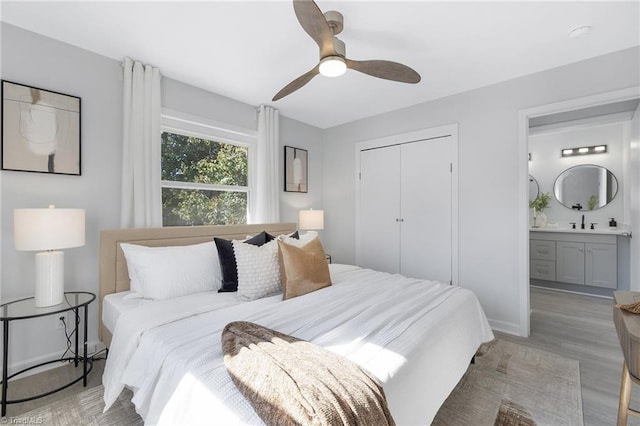 bedroom with ceiling fan, light hardwood / wood-style flooring, a closet, ensuite bath, and sink