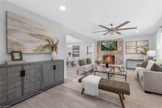 living room featuring light hardwood / wood-style floors, a brick fireplace, and ceiling fan with notable chandelier