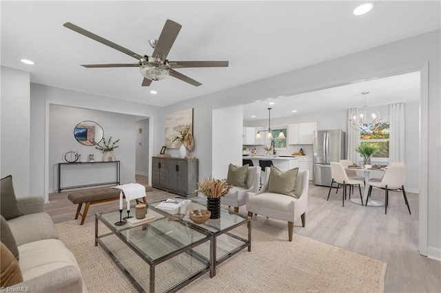 living room with sink, light hardwood / wood-style flooring, and ceiling fan with notable chandelier