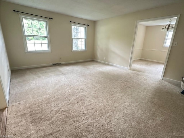 spare room featuring a notable chandelier, carpet floors, baseboards, and visible vents