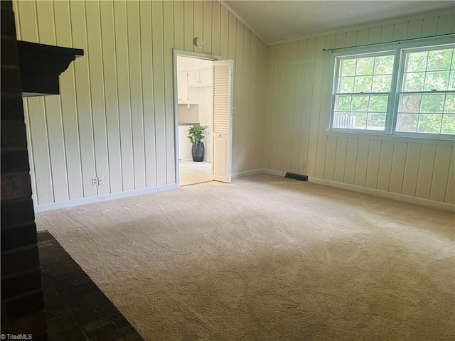 empty room with visible vents, baseboards, wood walls, light colored carpet, and ornamental molding
