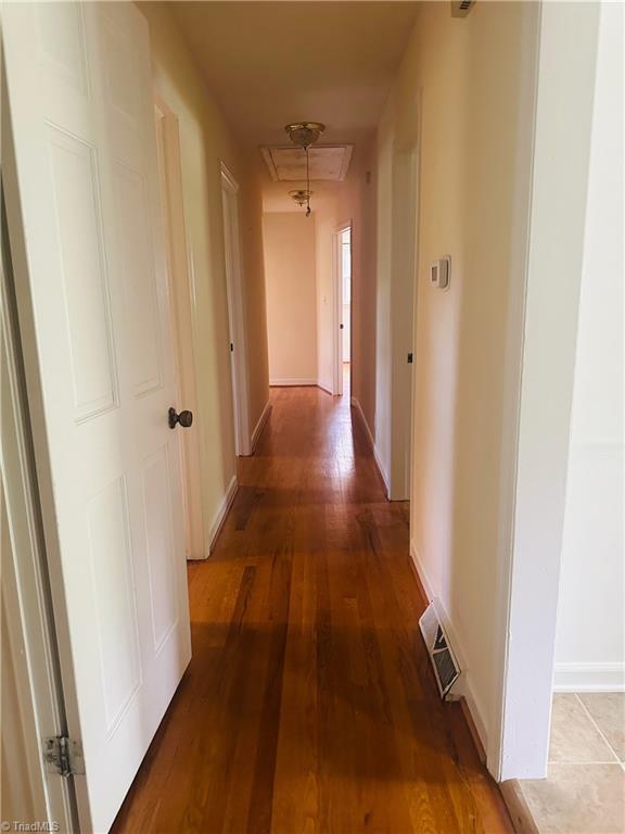 hallway featuring baseboards, visible vents, and wood finished floors