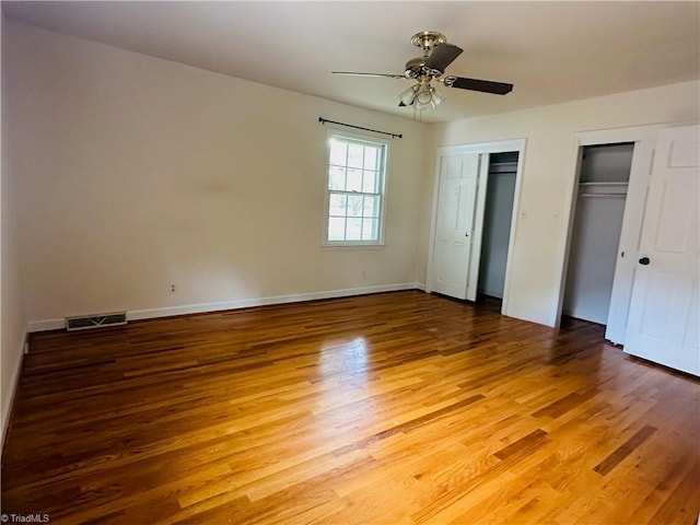 unfurnished bedroom with two closets, baseboards, light wood-type flooring, and visible vents