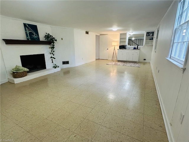 unfurnished living room featuring ornamental molding, a fireplace with raised hearth, baseboards, and visible vents