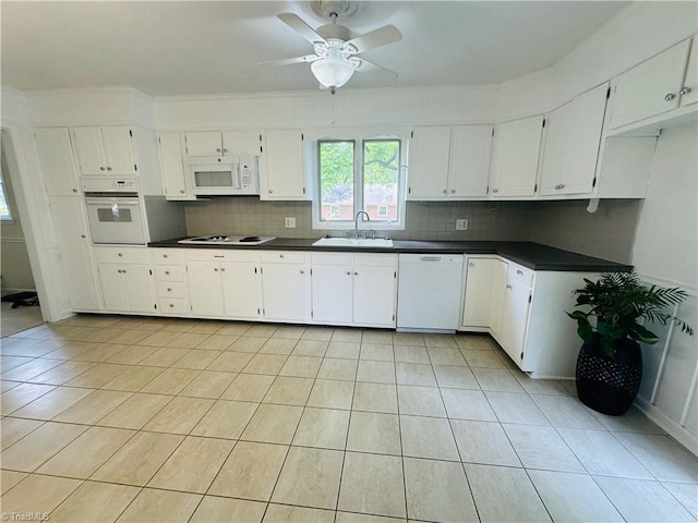 kitchen with light tile patterned floors, white appliances, a sink, dark countertops, and tasteful backsplash