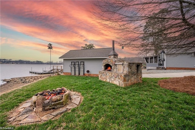 view of yard featuring a fire pit, an outdoor stone fireplace, a water view, a boat dock, and a patio area