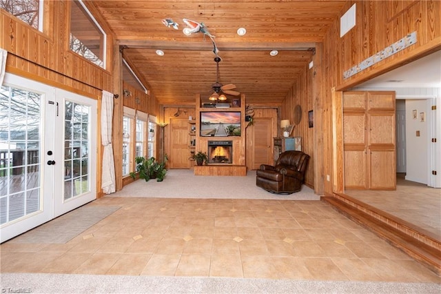 interior space with wooden ceiling, a warm lit fireplace, wooden walls, and high vaulted ceiling