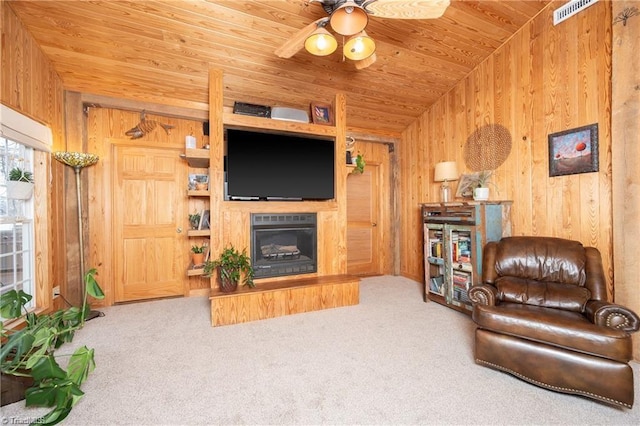 living area with carpet, wooden ceiling, a glass covered fireplace, and wooden walls