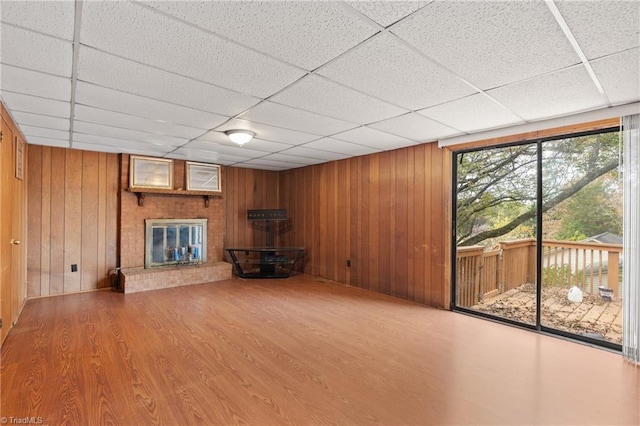 unfurnished living room with hardwood / wood-style floors, a paneled ceiling, wood walls, and a fireplace