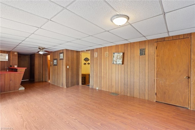 interior space with hardwood / wood-style flooring, a drop ceiling, wooden walls, and ceiling fan