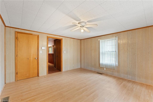 empty room with ceiling fan, wood walls, and light hardwood / wood-style flooring