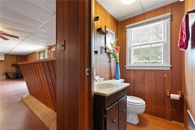 bathroom with toilet, a paneled ceiling, wooden walls, vanity, and hardwood / wood-style flooring