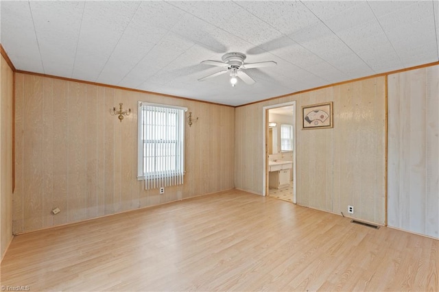 empty room with ceiling fan, wooden walls, and light hardwood / wood-style flooring