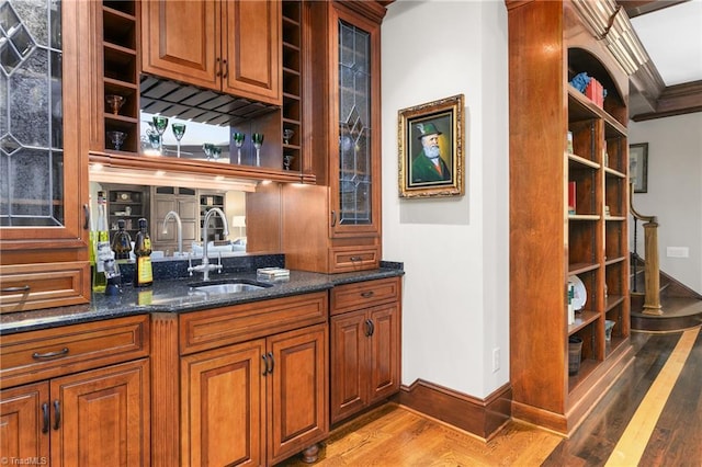 bar with crown molding, sink, dark stone countertops, and light hardwood / wood-style flooring