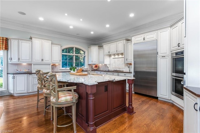 kitchen with a breakfast bar area, dark stone counters, a kitchen island with sink, stainless steel appliances, and crown molding