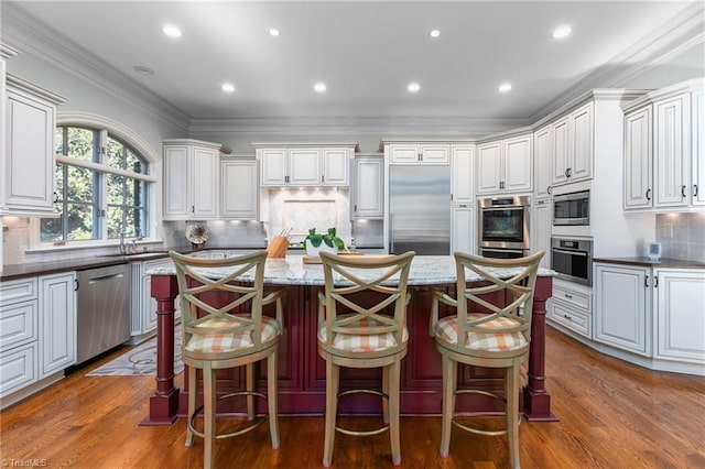 kitchen featuring built in appliances, white cabinets, a kitchen breakfast bar, and dark stone counters