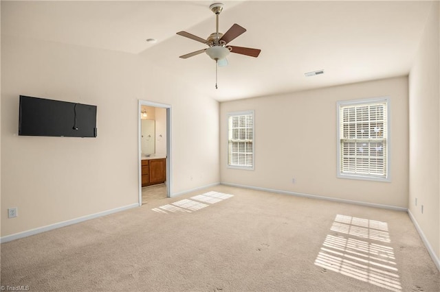 unfurnished bedroom featuring vaulted ceiling, connected bathroom, light colored carpet, and ceiling fan