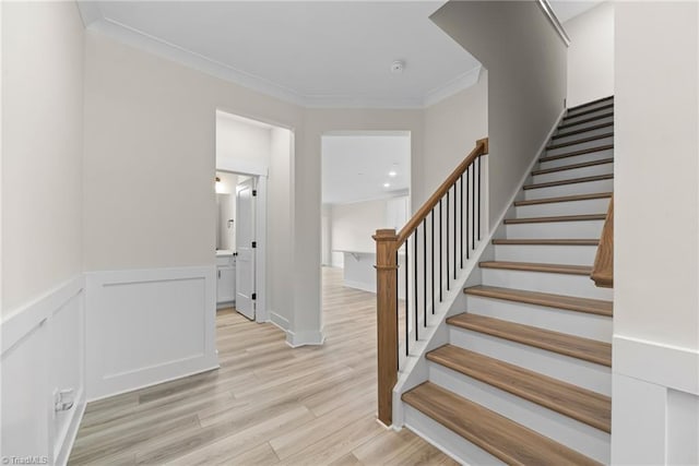 stairway featuring wood finished floors, crown molding, and a wainscoted wall