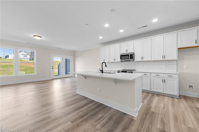 kitchen with appliances with stainless steel finishes, light countertops, light wood-type flooring, white cabinets, and recessed lighting