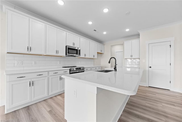 kitchen with stainless steel appliances, a sink, light wood-style floors, tasteful backsplash, and an island with sink