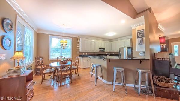 5110 Hartridge Way, Greensboro, NC 27407 - kitchen with appliances with stainless steel finishes, crown molding, dark countertops, a peninsula, and a breakfast bar
