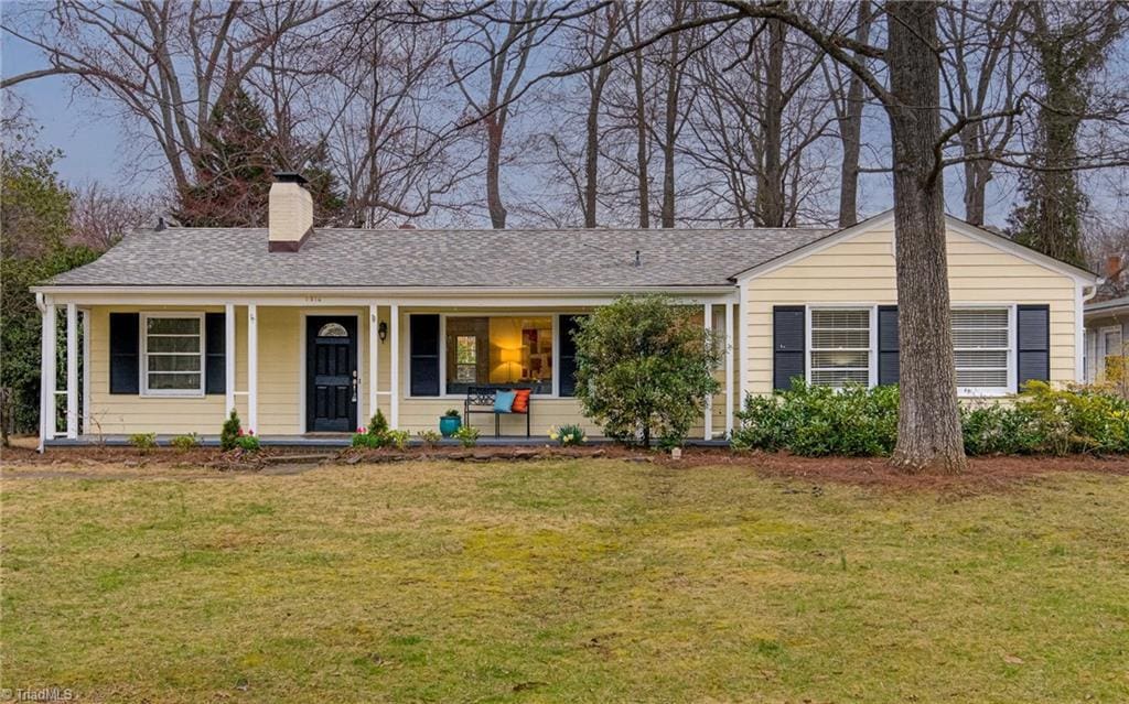 ranch-style home with a chimney, covered porch, and a front lawn