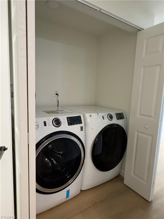 clothes washing area with washing machine and clothes dryer and light hardwood / wood-style floors