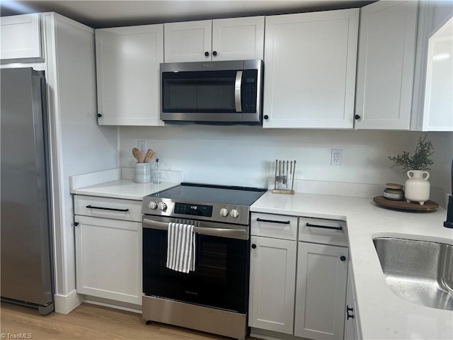 kitchen featuring appliances with stainless steel finishes, sink, white cabinets, and light hardwood / wood-style floors