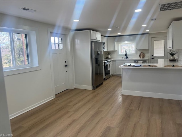 kitchen with sink, light hardwood / wood-style flooring, white cabinets, stainless steel appliances, and backsplash