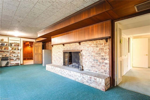 unfurnished living room with built in features, light colored carpet, a brick fireplace, and wood walls