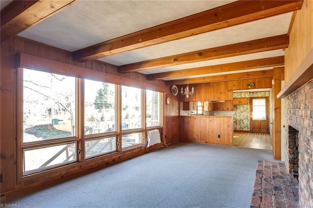 unfurnished living room with light carpet, wooden walls, a brick fireplace, and beam ceiling