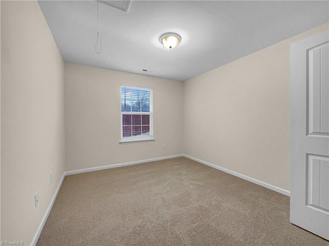 carpeted empty room featuring baseboards and attic access