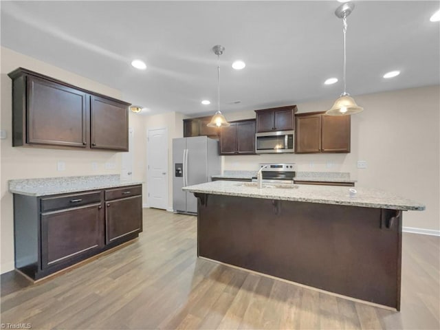 kitchen with a kitchen bar, dark brown cabinets, light wood-type flooring, and appliances with stainless steel finishes