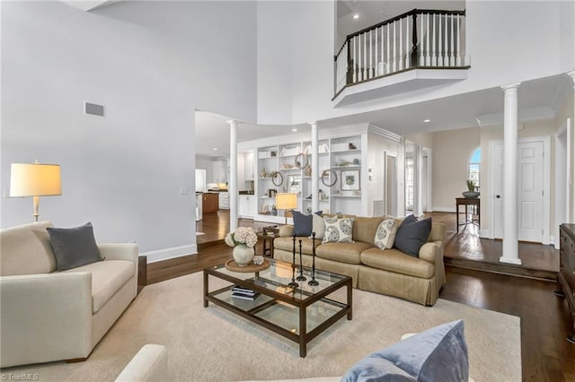 living room featuring ornate columns, a towering ceiling, and wood finished floors