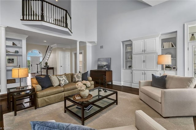 living area featuring baseboards, a high ceiling, decorative columns, and wood finished floors