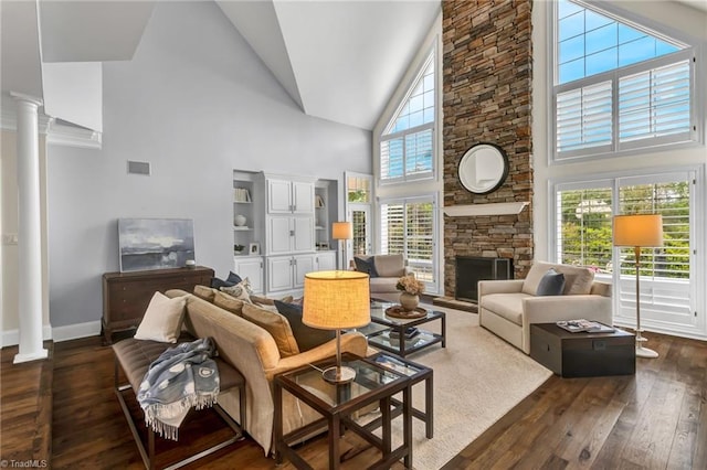 living area with visible vents, a stone fireplace, high vaulted ceiling, ornate columns, and dark wood finished floors