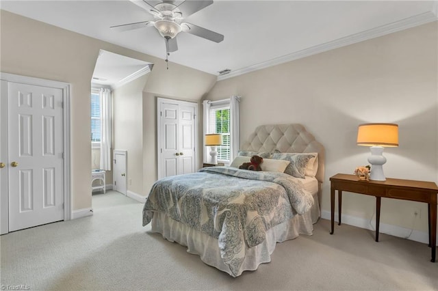 carpeted bedroom featuring a ceiling fan, visible vents, crown molding, baseboards, and multiple closets