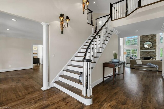 stairs featuring decorative columns, wood finished floors, a stone fireplace, baseboards, and recessed lighting