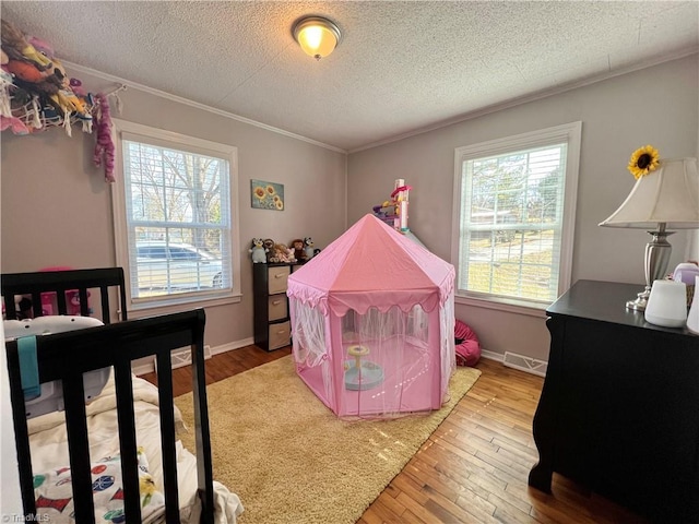 bedroom with multiple windows, visible vents, wood finished floors, and ornamental molding