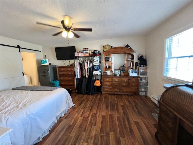 bedroom featuring a barn door, a ceiling fan, wood finished floors, a textured ceiling, and a baseboard heating unit