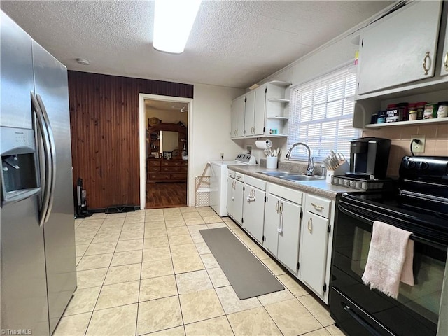 kitchen featuring a sink, black electric range oven, open shelves, washer / clothes dryer, and stainless steel fridge