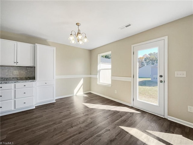 unfurnished dining area with an inviting chandelier, wood walls, and dark hardwood / wood-style flooring